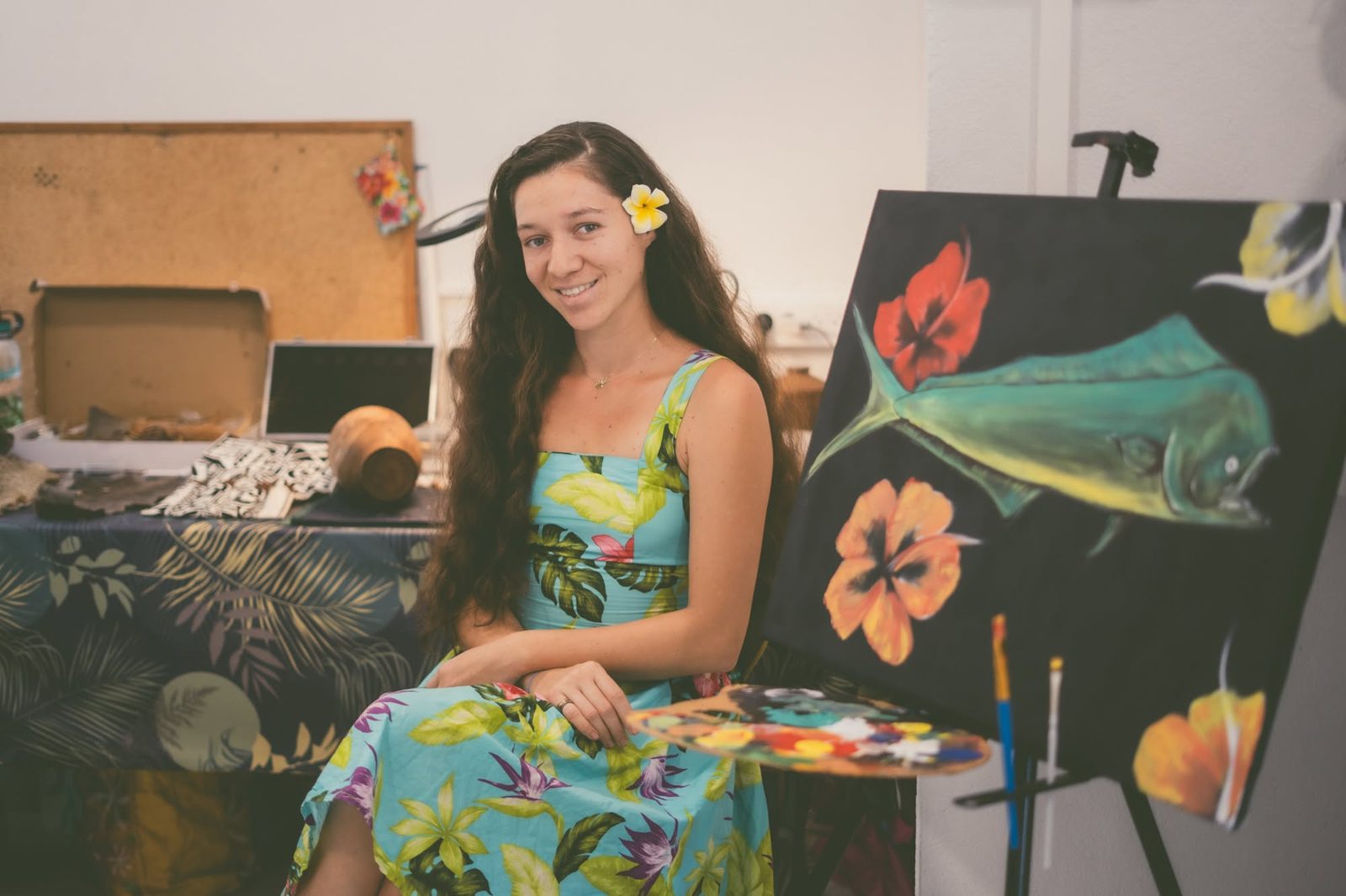 L'artiste dans son atelier, devant une toile représentant un mahi-mahi et des hibiscus